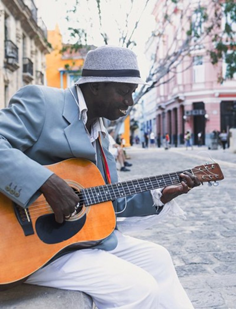 Ein Mann spielt akustische Gitarre an einer Straßenecke und verbreitet karibisches Flair.