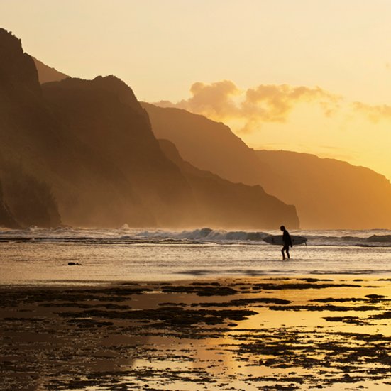 Eine Person läuft am Strand von Hawaii mit einem Surfbrett unter dem Arm.