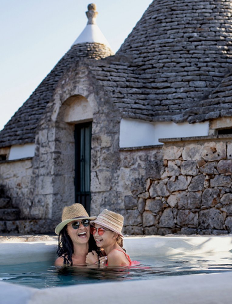 Eine Mutter vergnügt sich mit ihrer Tochter im Swimmingpool vor einem Trulli-Haus in Alberobello.