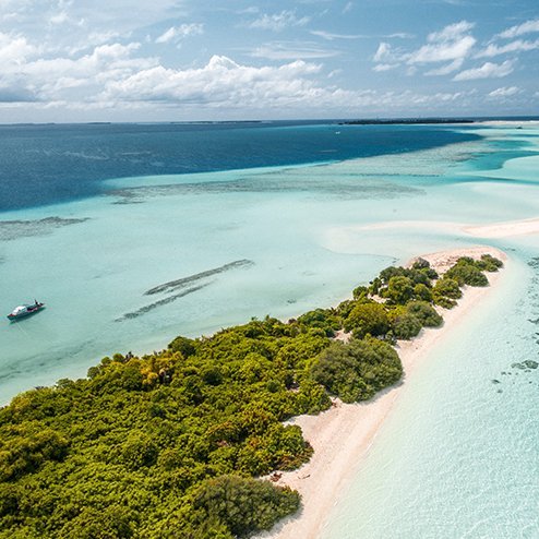 Luftaufnahme einer tropischen Insel auf den Malediven mit weissem Sand und blauem Wasser.