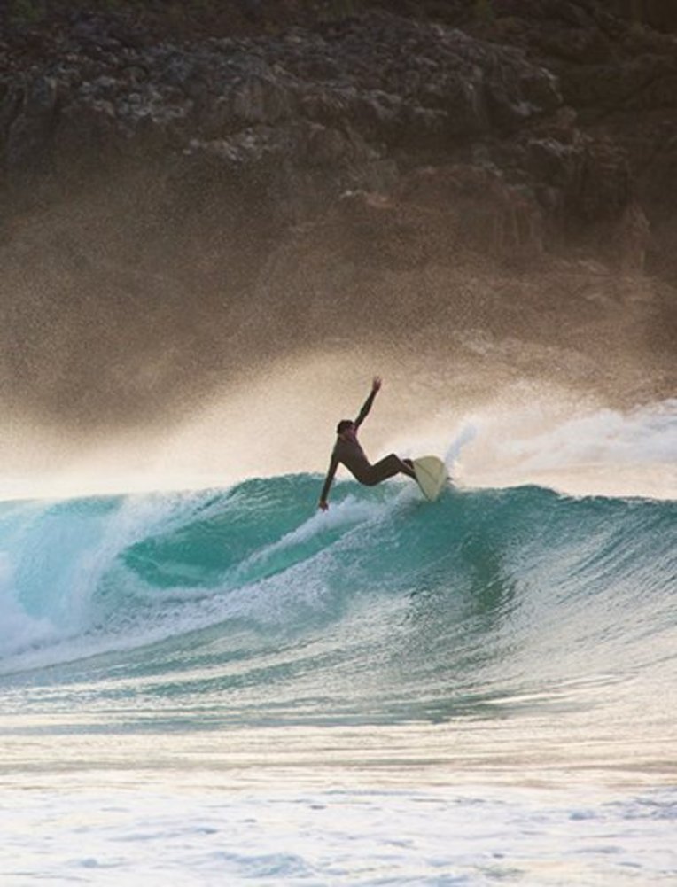 Surfer reitet eine Welle auf Fuerteventura, umgeben von klarem Wasser und strahlendem Himmel.