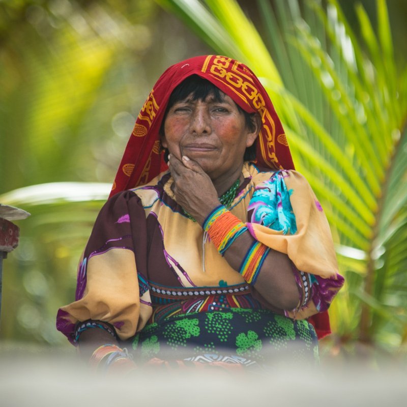 Eine indigene Frau aus Panama sitzt auf einer Bank und stützt ihr Kinn mit der Hand.
