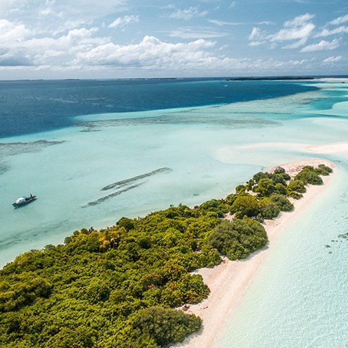 Vue aérienne d'une île tropicale des Maldives avec du sable blanc et de l'eau bleue.