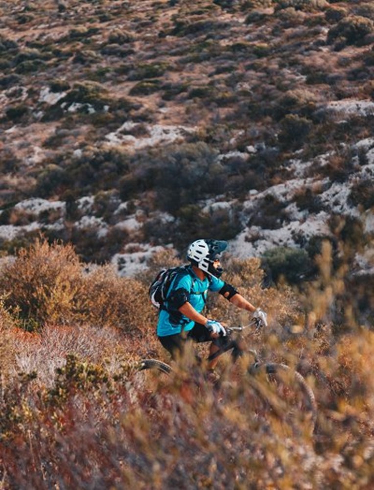 Eine Person fährt mit dem Mountainbike auf einem Trail in Sardinien, umgeben von grüner Natur und Bergen.