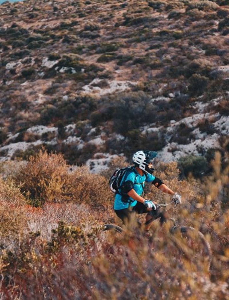 Eine Person fährt mit dem Mountainbike auf einem Trail in Sardinien, umgeben von grüner Natur und Bergen.