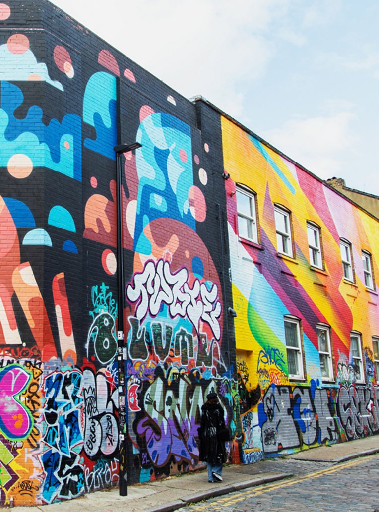 Ein Mann geht eine Strasse entlang, vorbei an einem grossen, bunten Wandgemälde in London.