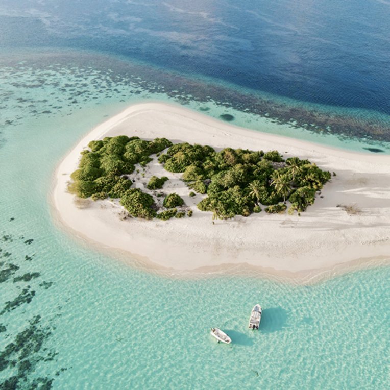 Luftaufnahme einer maledivischen Insel mit einem Boot im Wasser, umgeben von klarem, blauem Ozean.