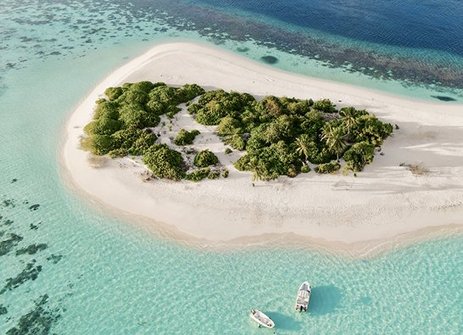 Luftaufnahme einer maledivischen Insel mit einem Boot im Wasser, umgeben von klarem, blauem Ozean.