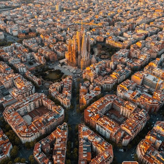 Luftaufnahme von Barcelonas Stadtbild bei Sonnenuntergang, mit warmen Farben und silhouettierten Gebäuden.