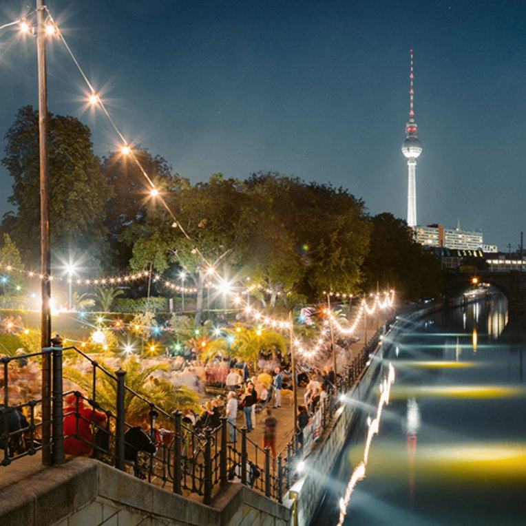  Ein Fluss in Berlin mit einer beleuchteten Brücke, die die nächtliche Szenerie erhellt.