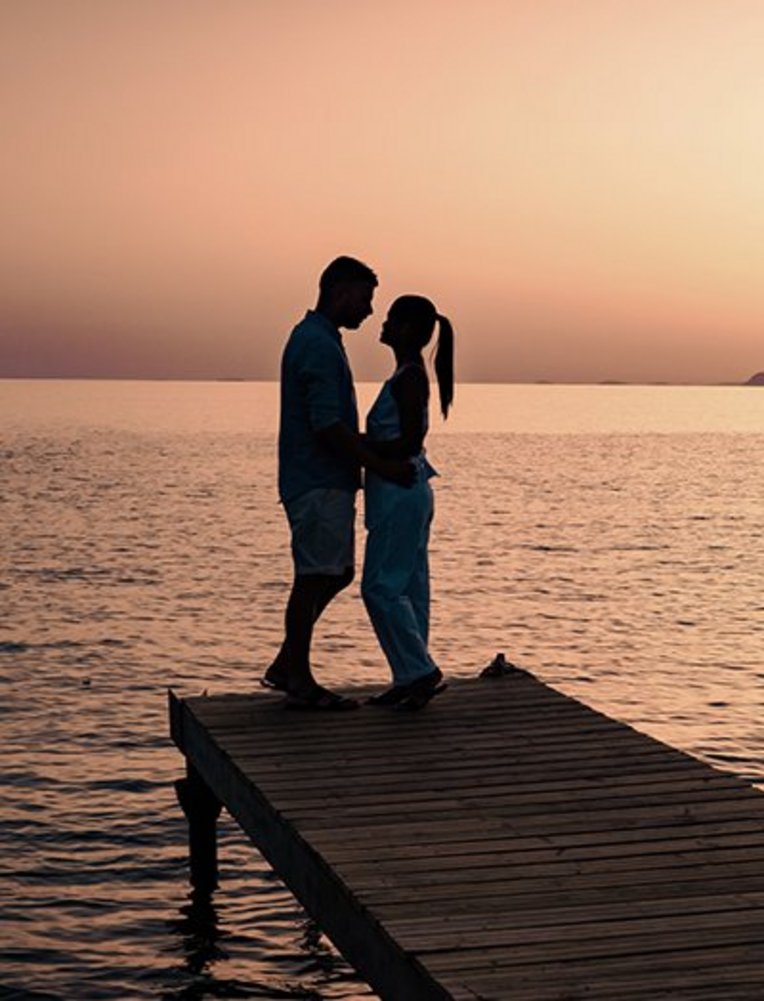 Ein Paar steht auf einem Steg bei Sonnenuntergang, romantische Stimmung während ihrer Hochzeitsreise auf Kreta.