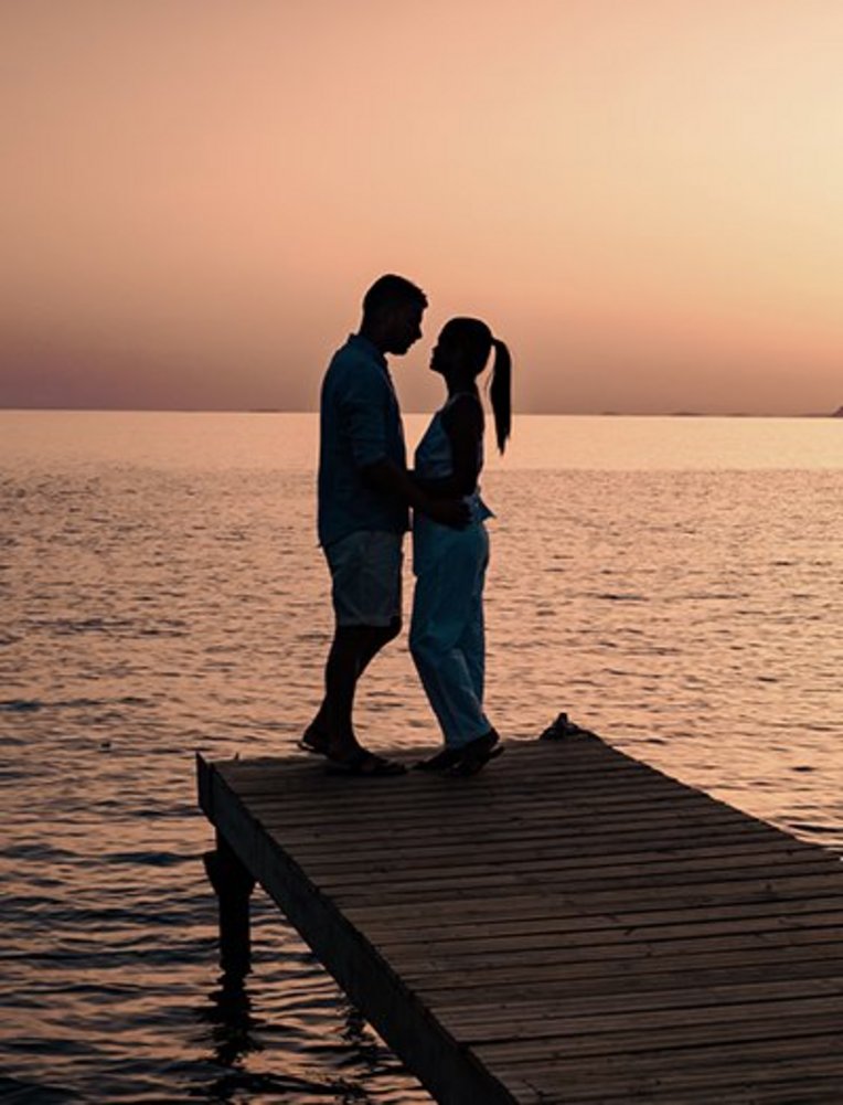 Un couple se tient sur une jetée au coucher du soleil, ambiance romantique pendant leur lune de miel en Crète.