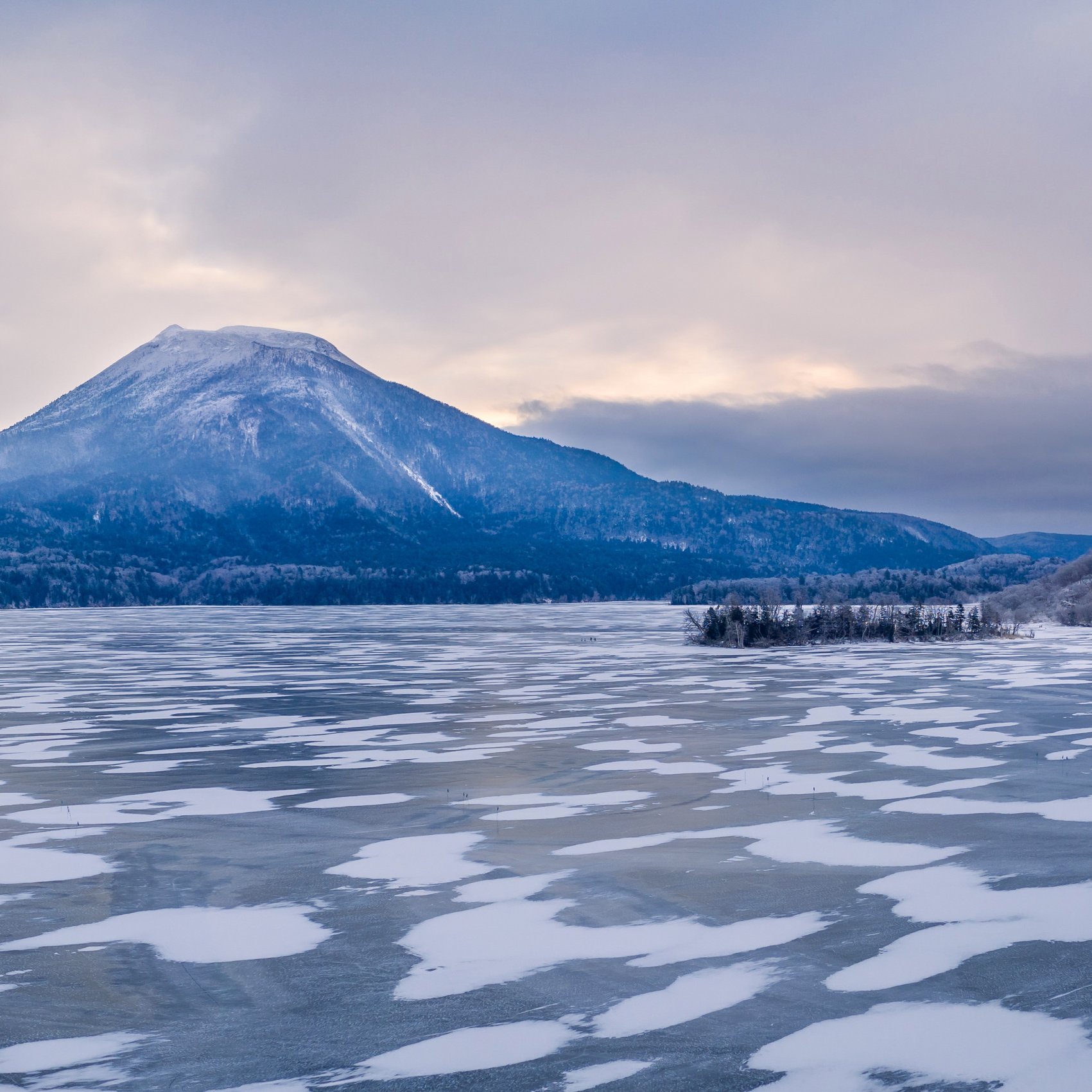 Eisbedeckter See mit verschneitem Vulkan im Akan Nationalpark, Hokkaido