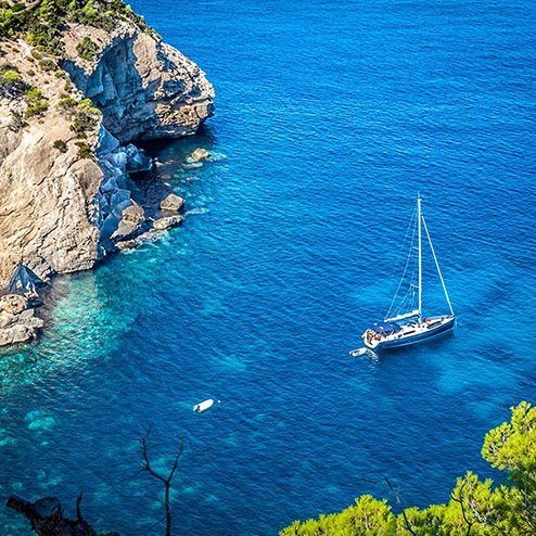  Un voilier se balance dans le bleu de l'océan, près d'une impressionnante falaise à Ibiza.