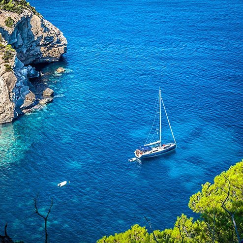  Ein Segelboot schaukelt im blauen Ozean, nahe einer beeindruckenden Klippe auf Ibiza.