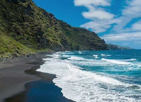Schwarzer Sandstrand mit Bergen im Hintergrund auf den Kanaren.