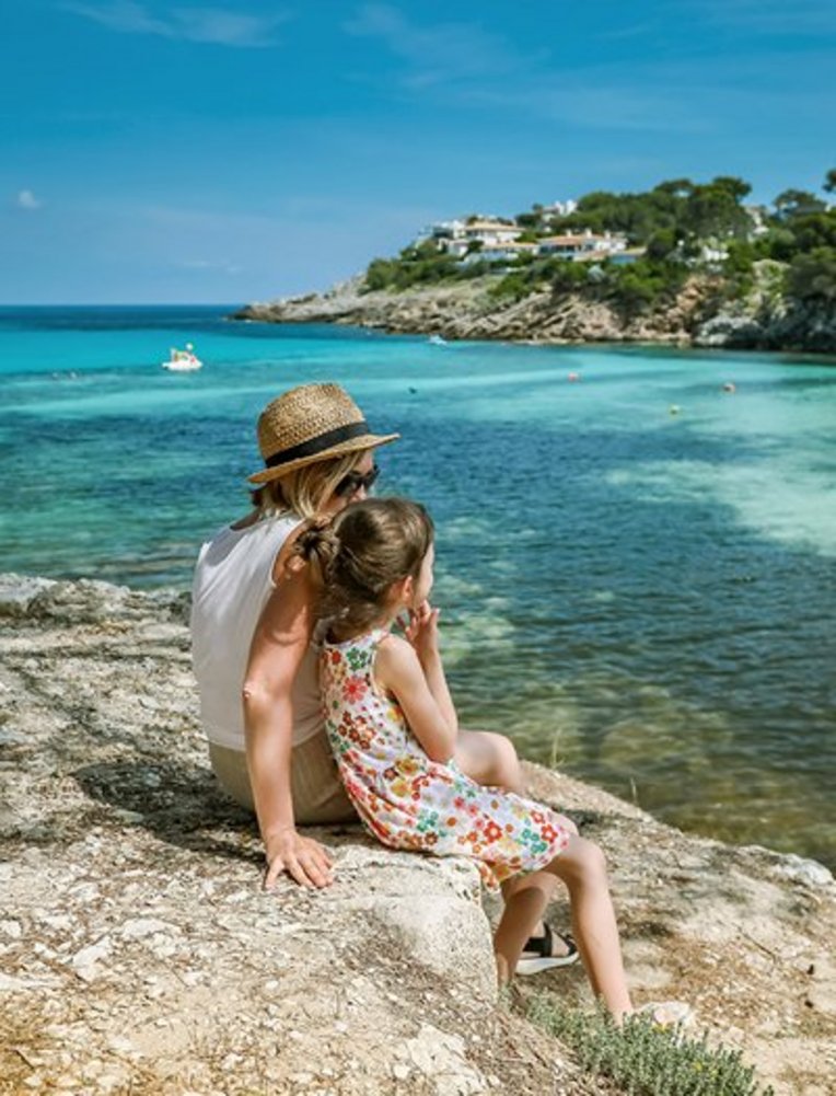 Eine Frau und ein Kind sitzen auf einem Felsen und blicken auf das Meer in Mallorca.