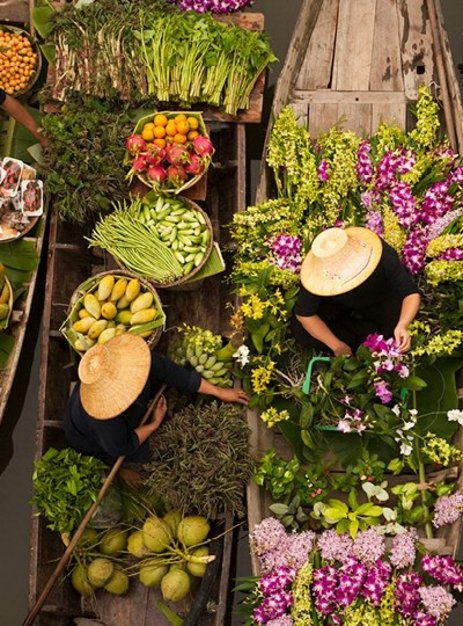 Eine Frau in einem Boot, umgeben von frischem Gemüse auf einem schwimmenden Markt in Thailand.