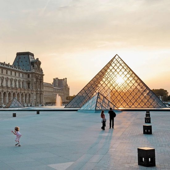 Der Louvre in Paris bei Sonnenuntergang, mit warmen Farben, die die berühmte Glaspyramide beleuchten.