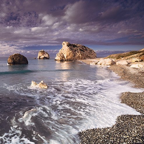 Ein Strand in Zypern mit Felsen und Wasser, unter einem bewölkten Himmel.