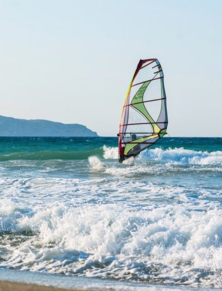 Windsurfer auf dem Wasser vor einem Strand in Kreta.