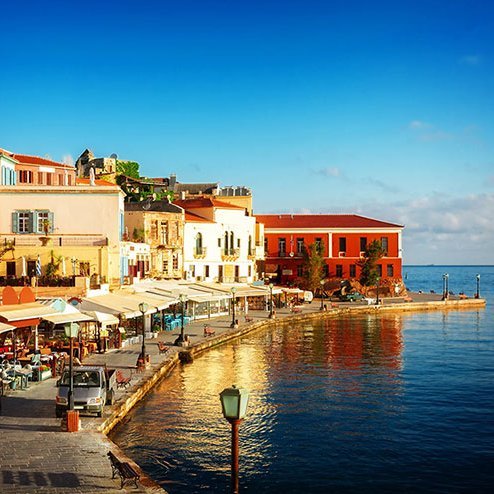 Vue sur le port et les bâtiments d'une ville en Crète, entourée d'eau cristalline et d'un ciel radieux.