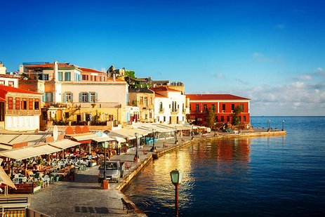 Ein malerischer Hafen mit bunten Gebäuden, gemütlichen Cafés und Restaurants am Wasser, während die Sonne die Szene in warmes Licht taucht und das ruhige Meer den Charme der Küste betont.