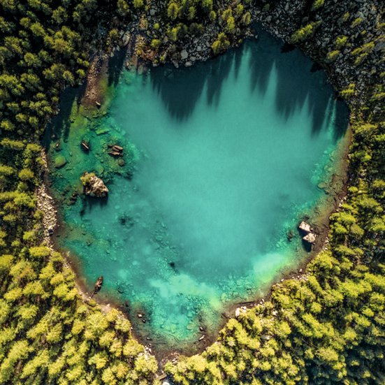 Herzförmiger See im Wald, umgeben von Bäumen und natürlicher Schönheit. Ein ruhiger Ort der Entspannung und Erholung.