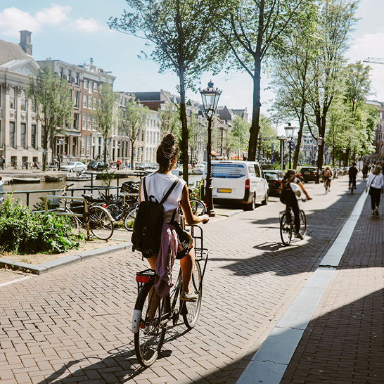 Eine Frau fährt mit dem Fahrrad eine gepflasterte Strasse in Amsterdam entlang.