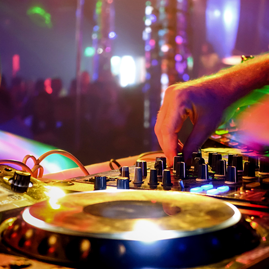 DJ mixt Musik auf einer Party in Berlin, umgeben von tanzenden Gästen und bunten Lichtern.