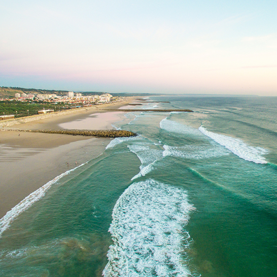 Ein Strand in Lissabon mit sanften Wellen und einem weiten Wasserblick.