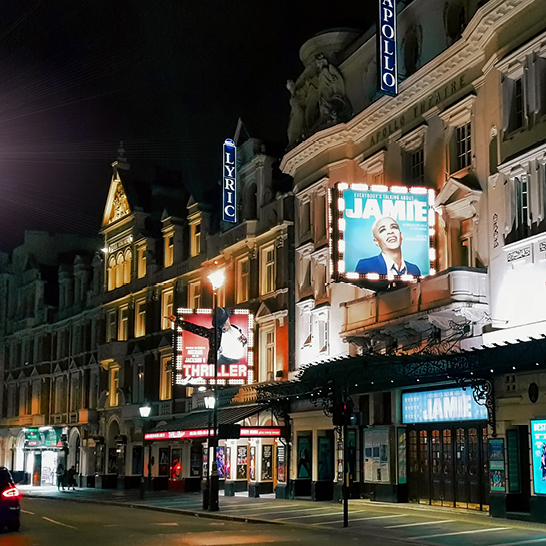 Eine Strasse in London bei Nacht, mit einem Theater und einem parkenden Auto im Vordergrund.