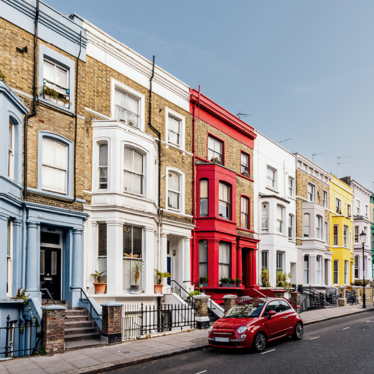 Ein rotes Auto parkt vor einer Reihe von bunten Häusern in London.