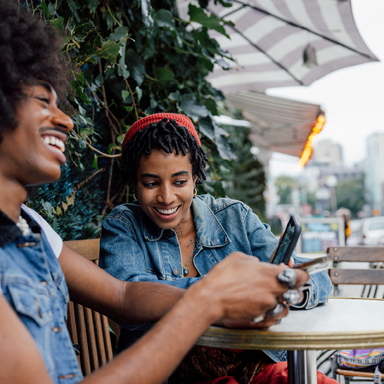  Ein Mann und eine Frau in NYC sitzen an einem Tisch und schauen gemeinsam auf ein Handy.