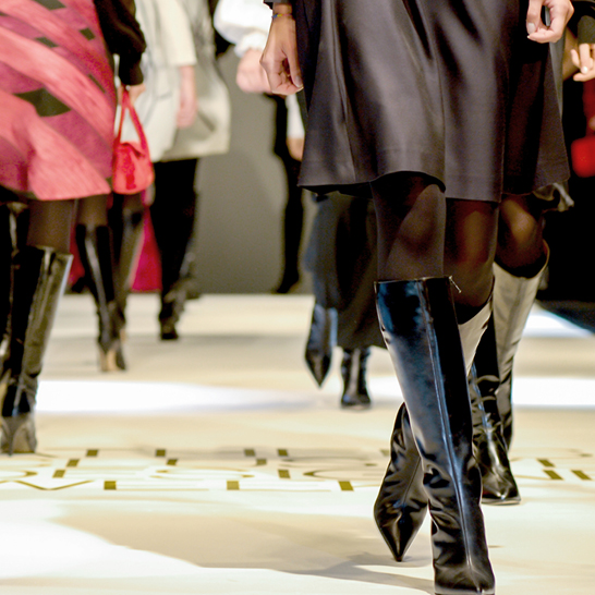 Eine Frau läuft auf einem Laufsteg in Paris und trägt schwarze Stiefel.