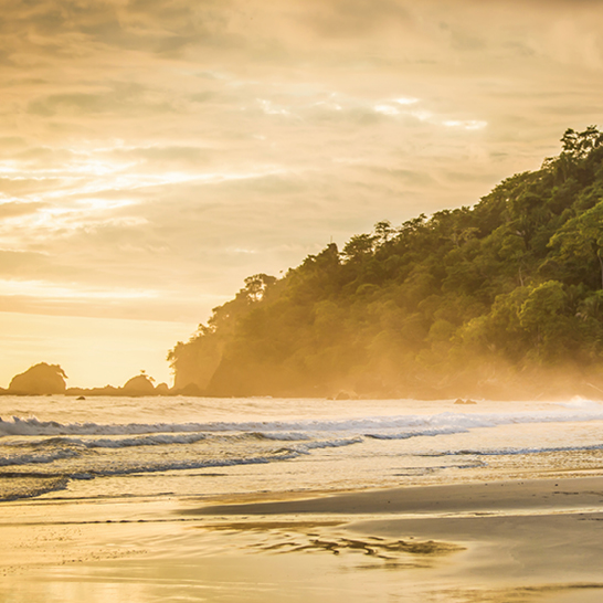 Un homme marche sur la plage de Manuel Antonio, Costa Rica, portant une planche de surf sous le bras.