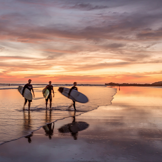 Trois surfeurs marchent sur la plage au coucher du soleil, sur la péninsule de Nicoya, Costa Rica.