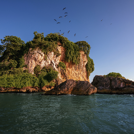Grosse Felsformation im Ozean mit Vögeln, die darüber fliegen, in Los Haitises, Dominikanische Republik.