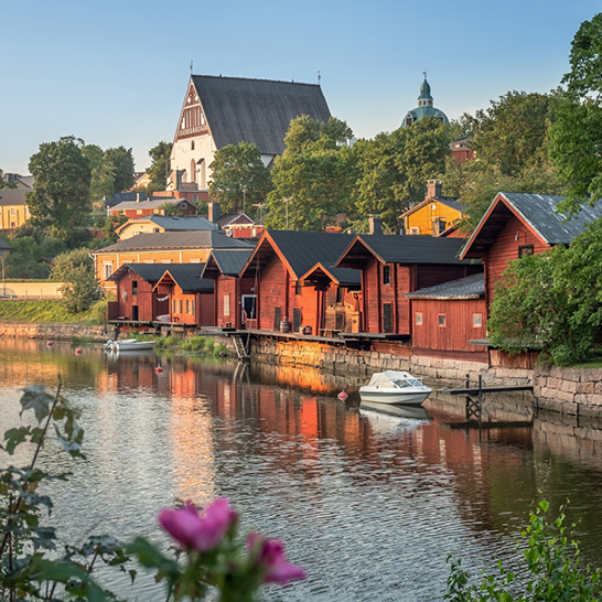 Ein Fluss in Porvoo mit einigen roten Häusern und einer Kirche im Hintergrund.