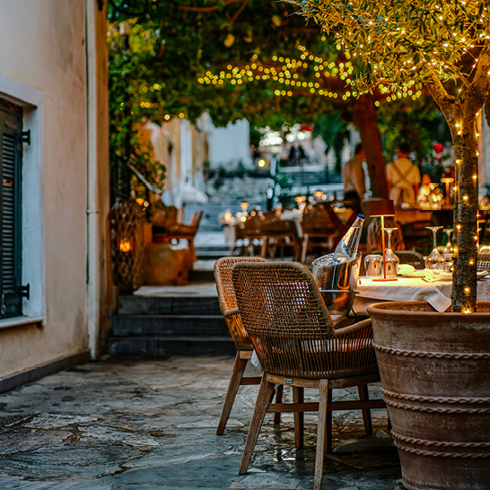 Restaurant mit Tischen und Stühlen im Freien, umgeben von griechischer Gastfreundschaft und mediterranem Flair.