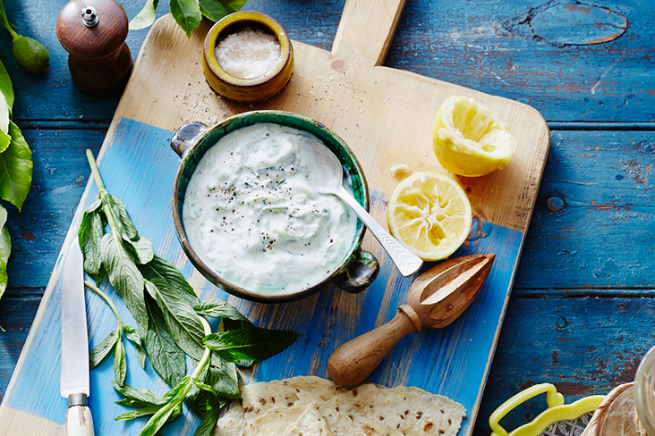 Ein Holzschneidebrett mit einer Schüssel Dip, einem Messer und einer Zitrone, inspiriert von griechischer Kultur.