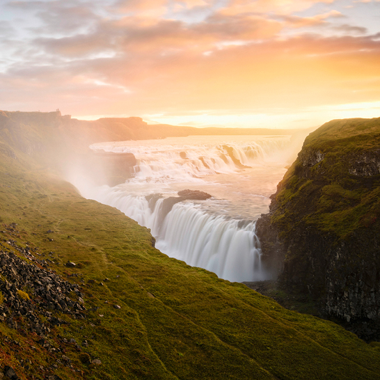 Gullfoss Wasserfall in Island bei Sonnenuntergang, mit leuchtenden Farben und sprühendem Wasser, das in die Schlucht stürzt.