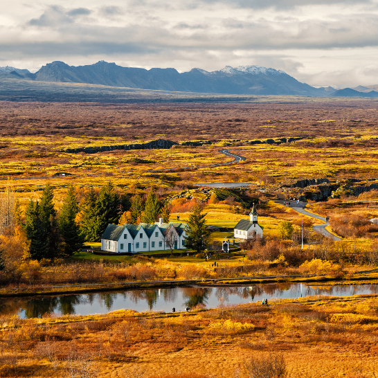 Ein ruhiger See mit glattem Wasser, umgeben von Bäumen und sanften Hügeln im Hintergrund.