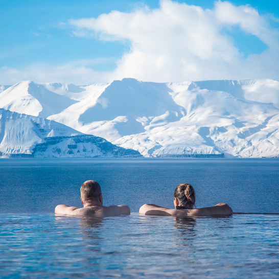 Zwei Personen relaxen im Wasser mit einem beeindruckenden Berg im Hintergrund.