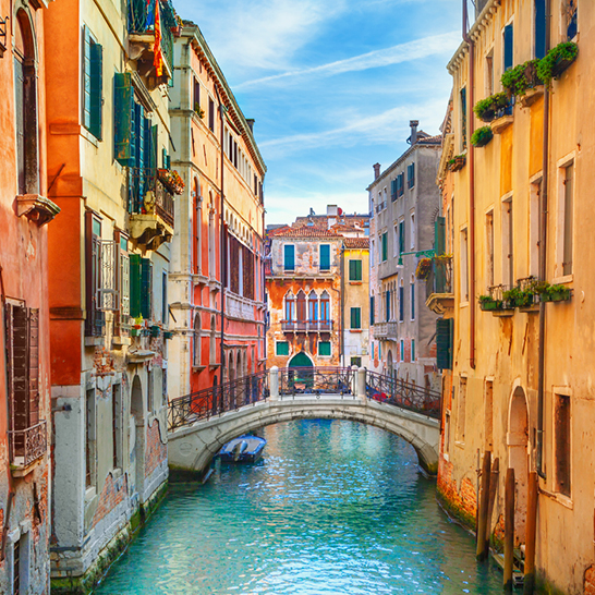  Ein Kanal in Venedig mit einer Brücke und einem Boot, das sanft auf dem Wasser schwimmt.