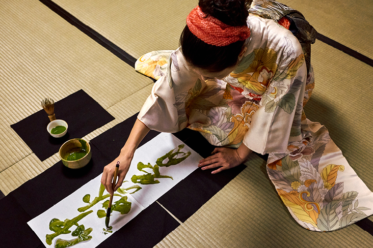  Eine Frau im Kimono malt auf ein Blatt Papier und konzentriert sich auf ihre Kunst.