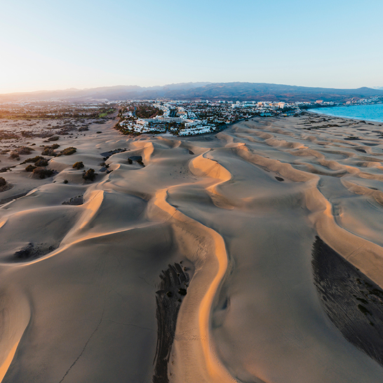 Sanddünen und Strand bei Sonnenuntergang auf Gran Canaria, mit warmen Farben und sanften Wellen im Hintergrund.
