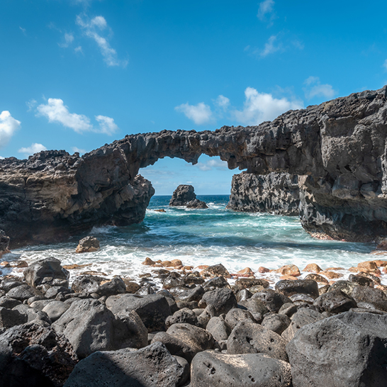 Felsiger Strand mit einem großen Bogen im Wasser, La Graciosa im Hintergrund.