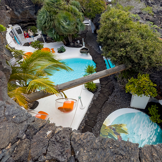 Ein Pool auf Lanzarote, umgeben von Palmen und Felsen, strahlt tropisches Flair und Entspannung aus.