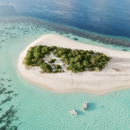Luftaufnahme einer maledivischen Insel mit einem Boot im Wasser, umgeben von klarem, blauem Ozean.